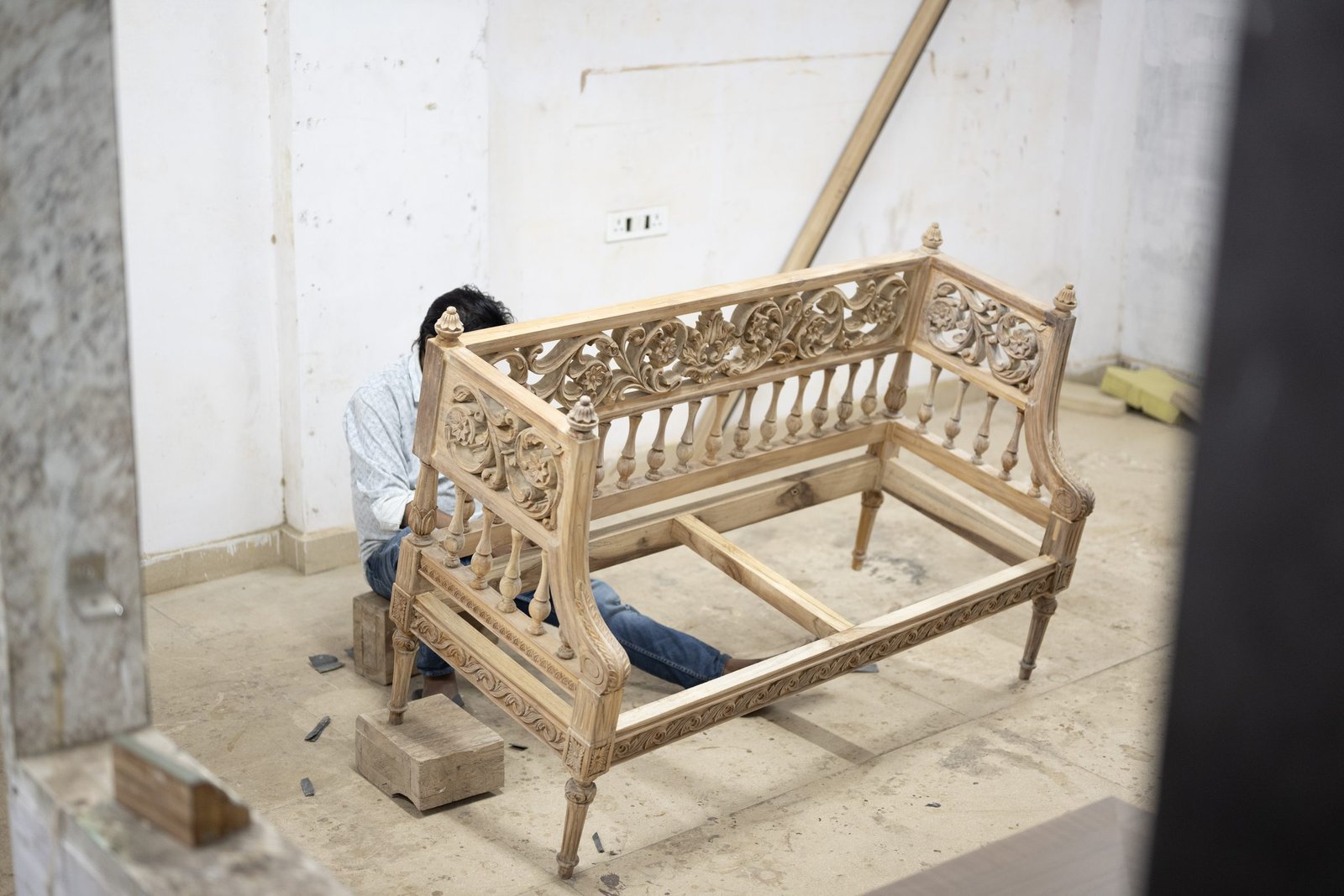 An intricately carved settee frame taking shape under a craftsman's hands