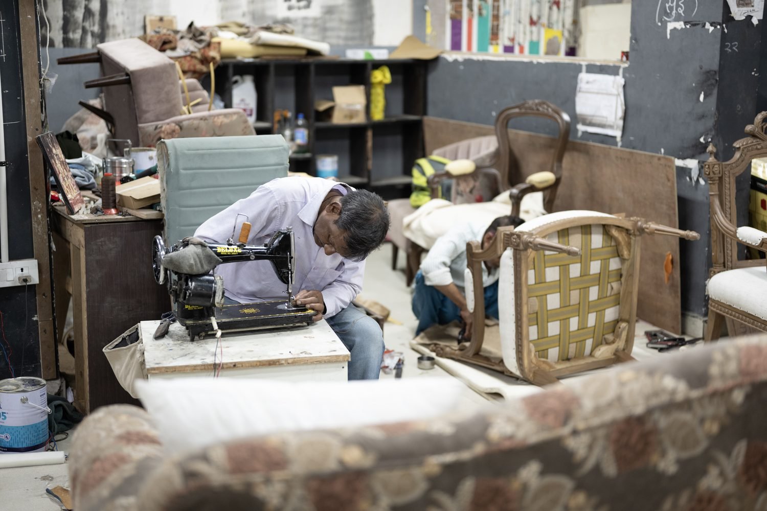An upholsterer webbing a chair seat beside an old sewing machine