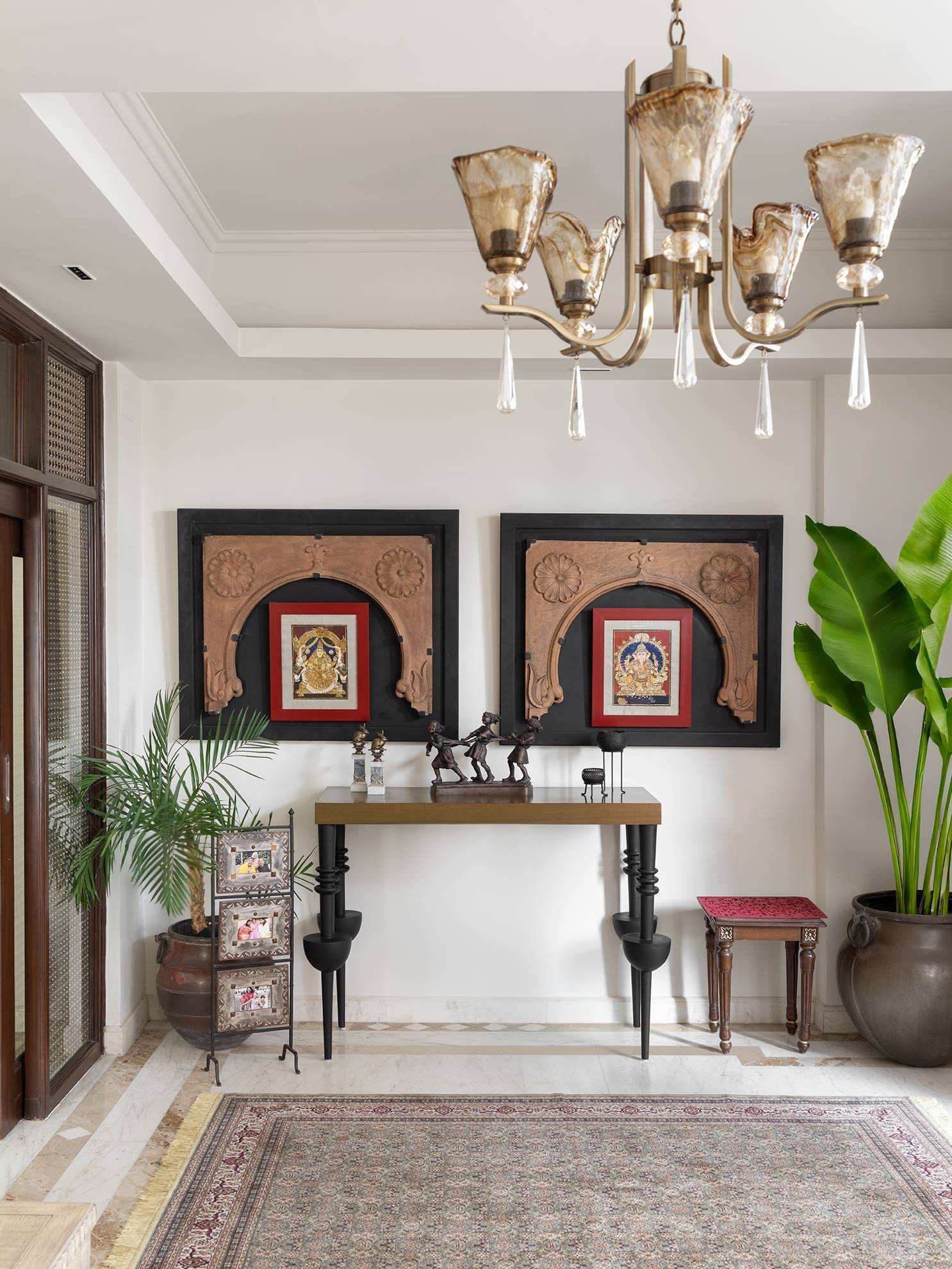 Residential foyer with a bespoke black console table, framed Tanjore paintings and a brass chandelier